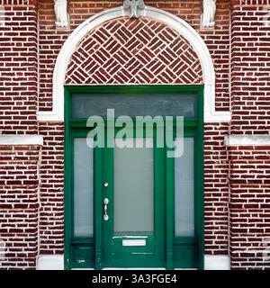 Grüne Tür mit Milchglas, die vor einer dekorativen roten Ziegelwand mit einem gemusterten Torbogen in Chicago steht. Stockfoto