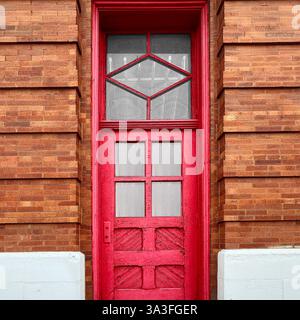 Urbane Vintage-Tür mit einer hohen, leuchtend roten Holztür mit charakteristischen geometrischen Fenstermustern, eingerahmt von detailliertem Mauerwerk. Stockfoto