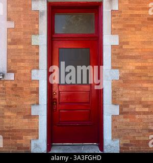 Rote Holztür mit Spiegelfenster, in einer orangen Ziegelwand mit dekorativen Steinverkleidungen in Chicago. Stockfoto