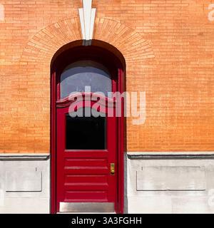 Rote Vintage-Tür mit bogenförmigem Heckfenster in einer orangen Ziegelwand mit dekorativen Steinakzenten in Chicago. Stockfoto