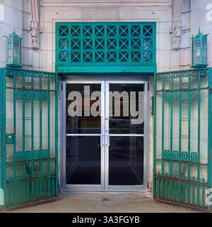 Ein historischer Bankeingang mit einer silbernen Glastür, eingerahmt von grünen Metalltüren und Gittern, in einer klassischen Steinfassade. Stockfoto