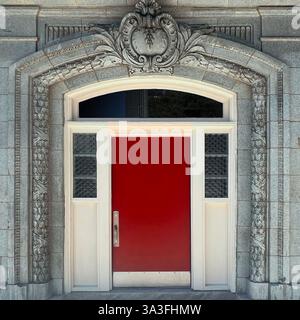 Die rote Tür wird von filigranen Steinschnitzereien und dekorativen architektonischen Details eingerahmt und schafft einen markanten Kontrast innerhalb einer historischen Gebäudefassade. Stockfoto
