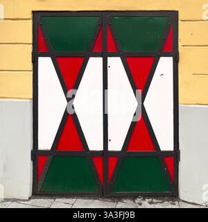 Metalltür mit geometrischen Mustern in Rot, weiß und Grün, vor einer gelben und grauen Wand in Warschau, Polen Stockfoto