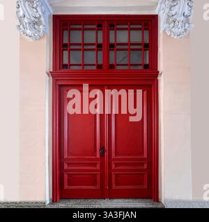 Rote Doppeltür mit komplizierten Zierleisten und einem Heckfenster, eingerahmt von verzierten Stuckdetails in einem historischen Gebäude in Łódź, Polen Stockfoto