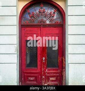 Eine verwitterte rote Holztür mit kunstvollen Schmiedearbeiten auf dem bogenförmigen Heckspiegel in einer hellen Fassade in den historischen Straßen von Warschau, Polen Stockfoto