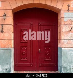 Eine große rote Holztür mit komplizierten Details in einem historischen bogenförmigen Eingang, die den architektonischen Charme der Warschauer Altstadt in Polen widerspiegelt Stockfoto