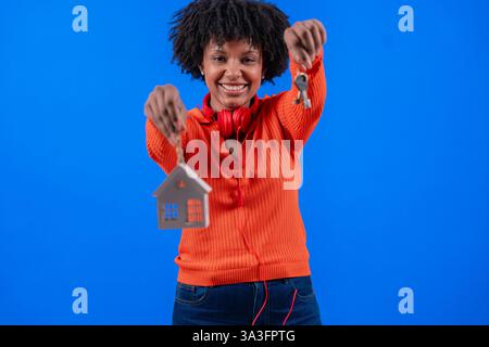 Afroamerikanerin, die Hausschlüssel und Hausmodel hält und selbstbewusst lächelt Stockfoto