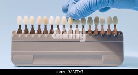 Nahaufnahme einer Hand mit Handschuhen, die eine Zahnfarbe aus einem Zahnfarbleitfaden auswählt, die für passende Veneers, Kronen und Restaurationen verwendet wird. Stockfoto