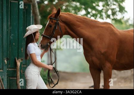 Die Frau hat einen Hut, Seitenansicht. Mit einem Pferd im Freien. Stockfoto
