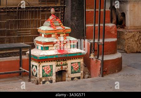 Kathmandu, Nepal - 11. Februar 2025 - Ein kleiner buddhistischer Tempel vor einem Gebäude in der Straße mit einer Ringelblumengirlande Stockfoto