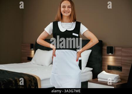 Posieren, stehen und lächeln. Das junge Zimmermädchen ist im Hotelzimmer. Stockfoto