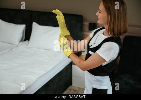 Tragen Sie die gelben Handschuhe. Das junge Zimmermädchen ist im Hotelzimmer. Stockfoto