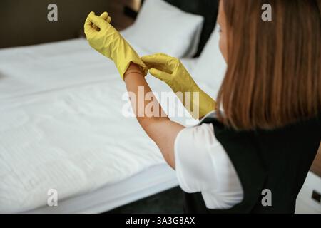 Tragen Sie die gelben Handschuhe. Das junge Zimmermädchen ist im Hotelzimmer. Stockfoto