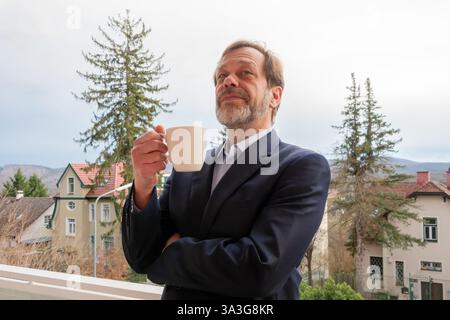 Ein selbstbewusster Geschäftsmann im klassischen Anzug entspannt sich bei einer Tasse Kaffee im Freien Stockfoto