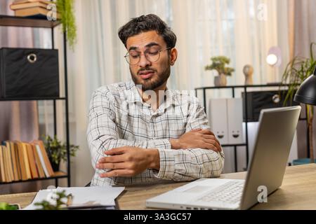 Müder indischer arabischer Geschäftsmann Guy Manager, der am Schreibtisch des Heimbüros mit Laptop sitzt und Schmerzen und Beschwerden im Ellenbogengelenk hat und schmerzhafte Hände massiert. Arthritis- und Bursitis-Konzepte. Stockfoto