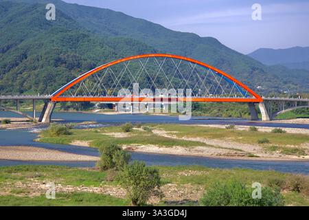 Gurye County, Südkorea - 3. Oktober 2021: Die Namdo Bridge mit ihrem leuchtenden rot-blauen Bogen überspannt den Seomjin River, umgeben von üppigem Grün Stockfoto
