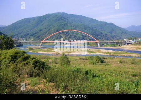 Gurye County, Südkorea - 3. Oktober 2021: Die Namdo Bridge mit ihrem markanten roten Bogen überspannt den Seomjin River vor einer Kulisse üppiger Berge Stockfoto