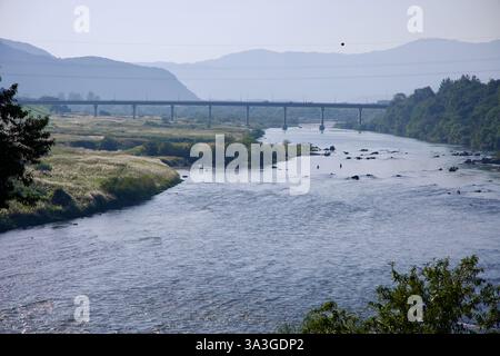 Gurye County, Südkorea - 3. Oktober 2021: Ein ruhiger Blick auf den Seomjin River mit einer Eisenbahnbrücke, die sich über das Tal erstreckt, während Fischer waten Stockfoto