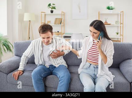 Junger Mann mit Brustschmerzen und Herzinfarkt, der auf dem Sofa zu Hause mit seiner Frau sitzt Stockfoto