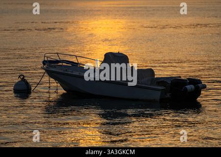 Boot bei Sonnenuntergang mit goldenen Reflektionen auf ruhigem Wasser in Varenna, Comer See, Italien Stockfoto