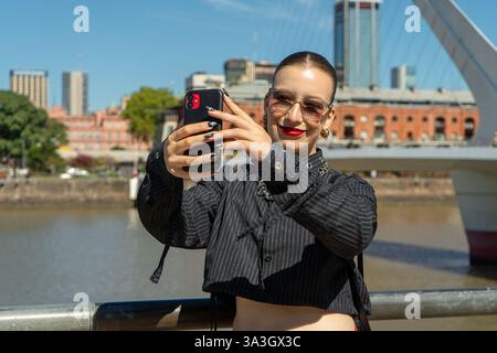 Fashion Influencer macht ein Selfie in puerto madero, buenos aires, mit seiner modernen Brücke und Stadtlandschaft Stockfoto