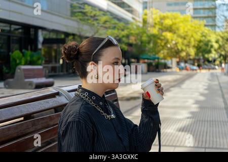 Geschäftsfrau, die eine Kaffeepause genießt und auf einer Bank in einer modernen Stadtumgebung sitzt Stockfoto
