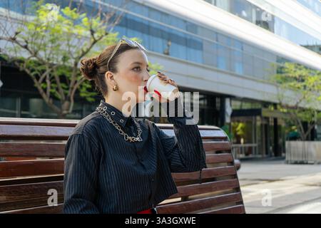 Geschäftsfrau genießt Kaffee während der Pause, sitzt auf einer Bank im Stadtzentrum Stockfoto
