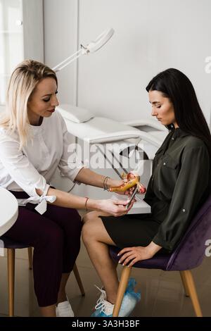 Gynäkologe wendet das Uterusmodell auf junge Frauen an und erläutert am Beispiel die Gebärmutterstruktur. Gynäkologische Sprechstunde über Beschwerden, gynäkologisch Stockfoto