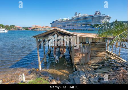 Ein kleines Ankerboot in Flowers Bay, Roatan, Honduras, mit einem großen Kreuzfahrtschiff im Hintergrund Stockfoto