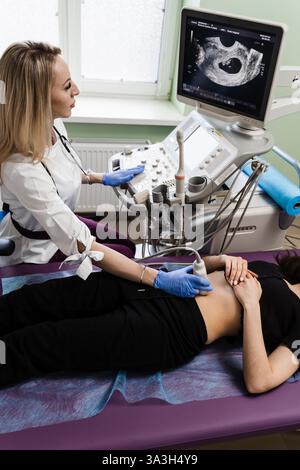 Schwangerschaft und Mutterschaft. Gynäkologe führt Ultraschalluntersuchungen für schwangere junge Frau in der frühen Schwangerschaftsperiode und schauen auf den Bildschirm im Krankenhaus Stockfoto