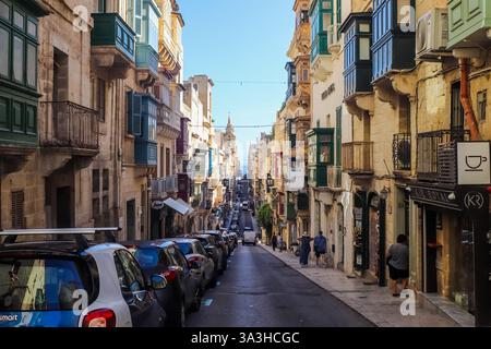 Valletta, Malta 27. September 2024, parkte Autos auf beiden Seiten einer schrägen Straße in Valletta, Malta, mit bunten Balkonen und dem Meer sichtbar in t Stockfoto
