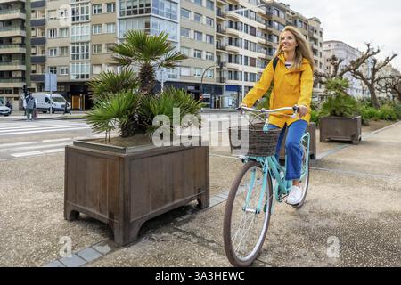 Junge Frau, die in der Stadt mit einem Oldtimer-Fahrrad fährt, in gelbem Regenmantel, die nachhaltige urbane Mobilität genießt Stockfoto
