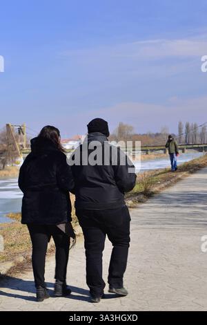 Zwei Leute, die an einem Wintertag am Ufer des Flusses Mures spazieren gehen und sich unterhalten Stockfoto