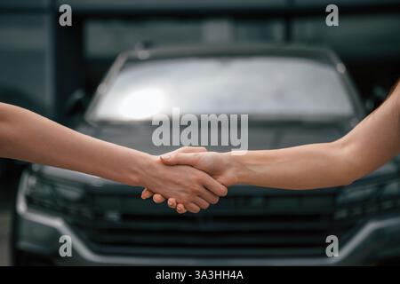 Seitliche Nahaufnahme des Handschlags von zwei Frauen gegen das Auto. Stockfoto