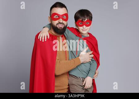 Vater und Sohn tragen Superheldenkostüme auf grauem Hintergrund Stockfoto