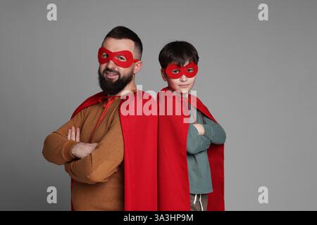 Vater und Sohn tragen Superheldenkostüme auf grauem Hintergrund Stockfoto