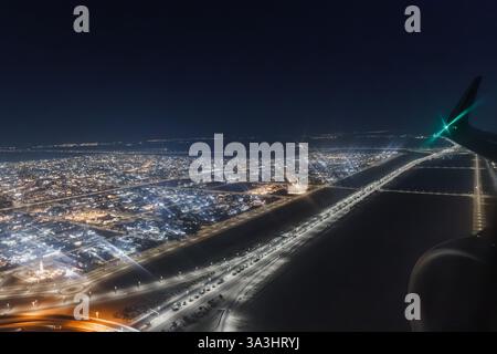 Flugzeugmotor und Flügel fliegen nachts über eine große beleuchtete Stadt, durch ein Flugzeugfenster gesehen Stockfoto