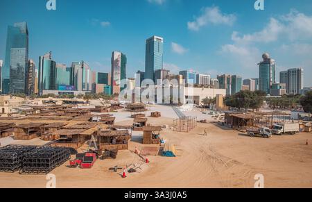 16. Januar 2025, Abu Dhabi, VAE: Bauarbeiter bauen traditionelle arabische Häuser mit einer Skyline aus modernen Wolkenkratzern im Hintergrund Stockfoto