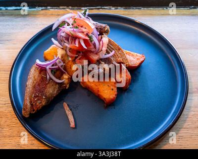 Chicharron de cerdo Schweinebauch langsam gekocht und frittiert mit Süßkartoffeln und Kartoffeln in tari-Sauce, peruanisches Gericht auf Teller im lokalen Restaurant Stockfoto