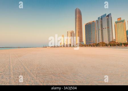 Malerischer Blick auf den Strand von Abu Dhabi Corniche bei Sonnenaufgang mit modernen Wolkenkratzern, die majestätisch im Hintergrund aufsteigen Stockfoto