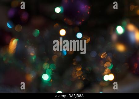Unscharfe bunte Bokeh-Lichter in Gold-, Grün- und Blautönen auf dunklem Hintergrund. Abstrakte festliche Urlaubsatmosphäre mit glühenden Kugeln Stockfoto