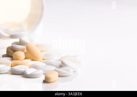 Eine Nahaufnahme verschiedener Pillen und Tabletten, die aus einem Behälter auf eine weiße Oberfläche verschüttet wurden. Stockfoto