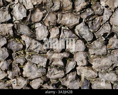 Nahaufnahme der Textur und des Musters in einer geknickten Feuersteinwand, die die Reihe sorgfältig verlegter Steine in dieser handwerklichen Wandbautechnik zeigt. Stockfoto