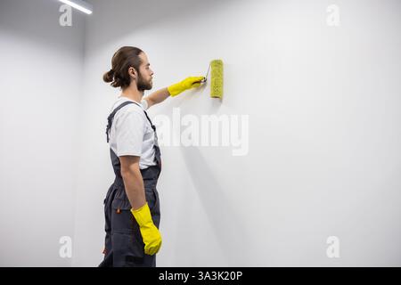Dunkelhaariger junger bärtiger Mann in gelben Handschuhen, der die Wand malte Stockfoto
