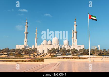 Malerische Aussicht auf die Scheich Zayed große Moschee unter einem klaren blauen Himmel mit der Flagge der Vereinigten Arabischen Emirate, die stolz winkt Stockfoto