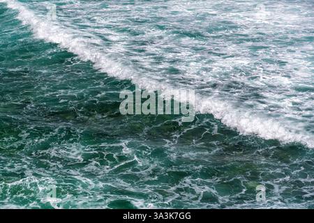 Smaragdgrüne Wellen brechen mit weißem Schaum im türkisfarbenen Ozean. Dynamische Meeresoberfläche mit rollenden türkisfarbenen Wellen. Faszinierendes Muster grüner Ozeanwellen Stockfoto