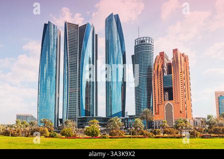 Malerische Aussicht auf die moderne Skyline von Abu Dhabi mit markanten Wolkenkratzern, die sich über einem üppig grünen Park im Vordergrund erheben Stockfoto