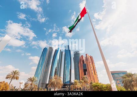 Flacher Blick auf die VAE-Flagge, die mit modernen Wolkenkratzern im Hintergrund in Abu Dhabi winkt Stockfoto