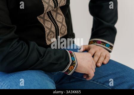 Nahaufnahme einer Person, die eine traditionelle dunkle Bluse mit detaillierter Stickerei auf Brust und Ärmeln trägt, kombiniert mit Blue Jeans. Stockfoto