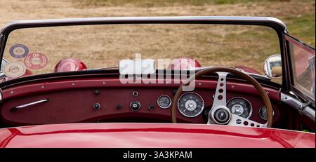 Blick aus dem Innenraum eines klassischen roten Austin Sprite Autos mit Vintage-Armaturenbrett und Holzlenkrad. Stockfoto